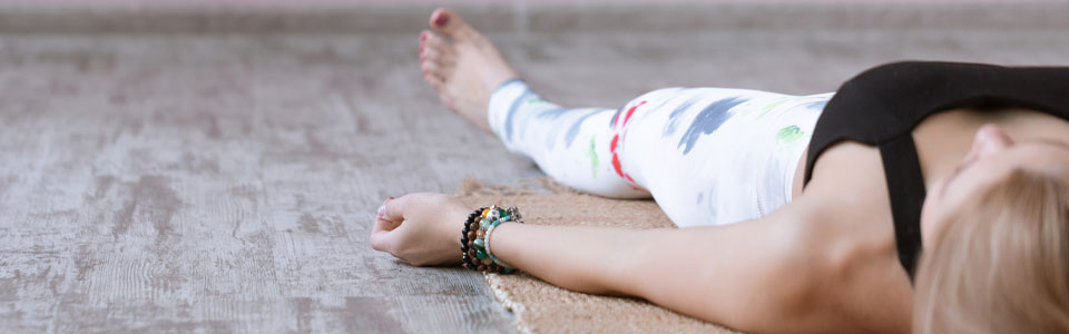 Person in Entspannungsposition auf Yogamatte Frau liegt auf dem Rücken auf einer Yogamatte, trägt bunte Leggings und Armbänder, entspannt sich