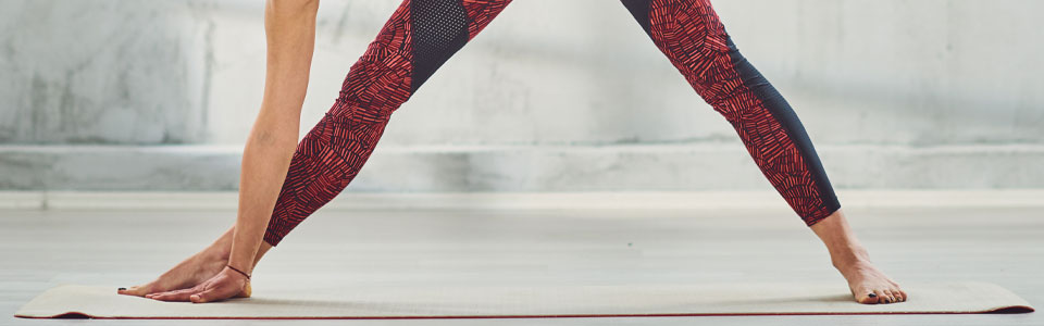 Person in Yoga-Pose auf Matte Nahaufnahme einer Person in einer Yoga-Position mit roten Leggings auf einer Matte