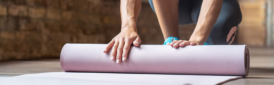Ausrollen einer Yogamatte Person rollt eine Yogamatte in einem Raum mit Holzboden aus