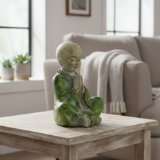 Figur eines meditierenden Kindes Tonfigur eines meditierenden Kindes in grüner Robe auf einem Holztisch im Wohnzimmer