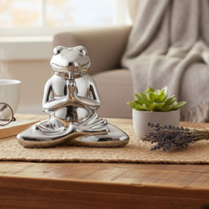 Froschstatue im Yoga-Sitz Silberne Froschstatue im Lotussitz neben einer Pflanze auf einem Tisch