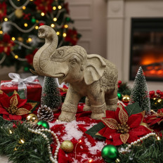 Elefant mit Weihnachtsdekoration Dekorative Elefantenskulptur umgeben von Weihnachtsdeko mit Baum und Kamin im Hintergrund.