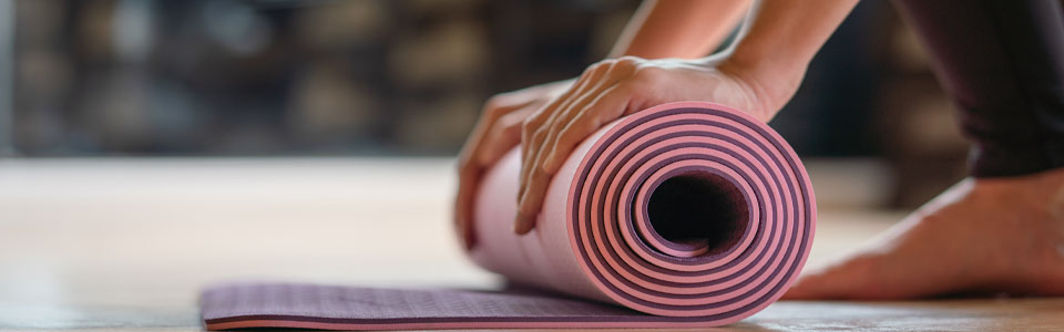 Nahaufnahme einer Hand, die eine Yogamatte auf dem Boden zusammenrollt