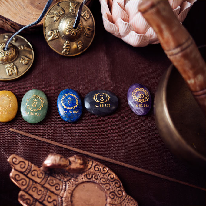Eine Sammlung von bunten Chakra-Steinen mit Symbolen und Zahlen, umgeben von Meditationsinstrumenten wie Glocken und einer Schale.