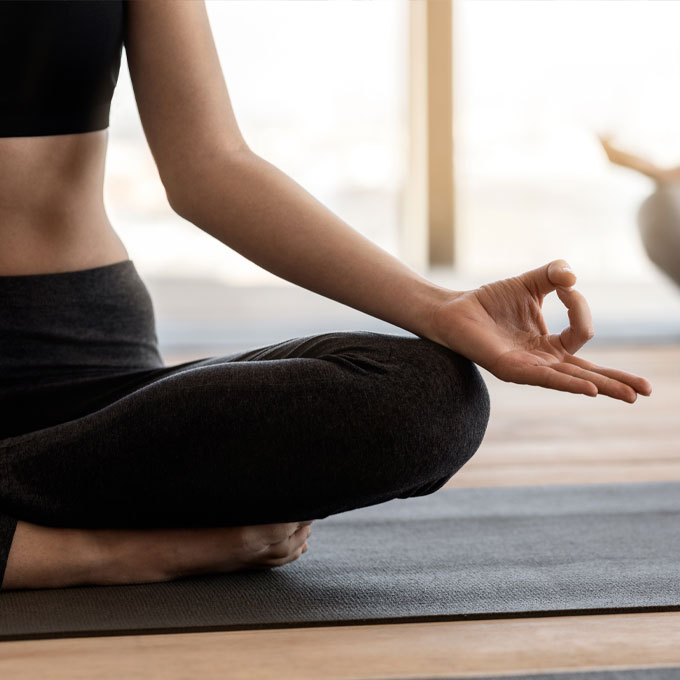 Nahaufnahme einer Person im Schneidersitz beim Yoga mit Hand in Meditationsgeste auf einer Yogamatte.
