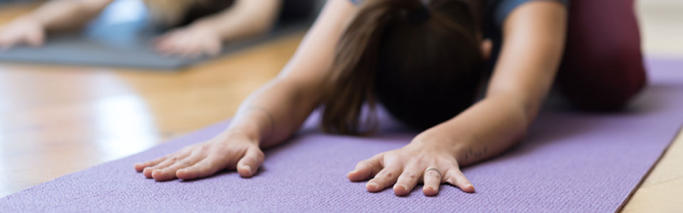 Eine Frau in der Kindhaltung auf einer lila Yogamatte