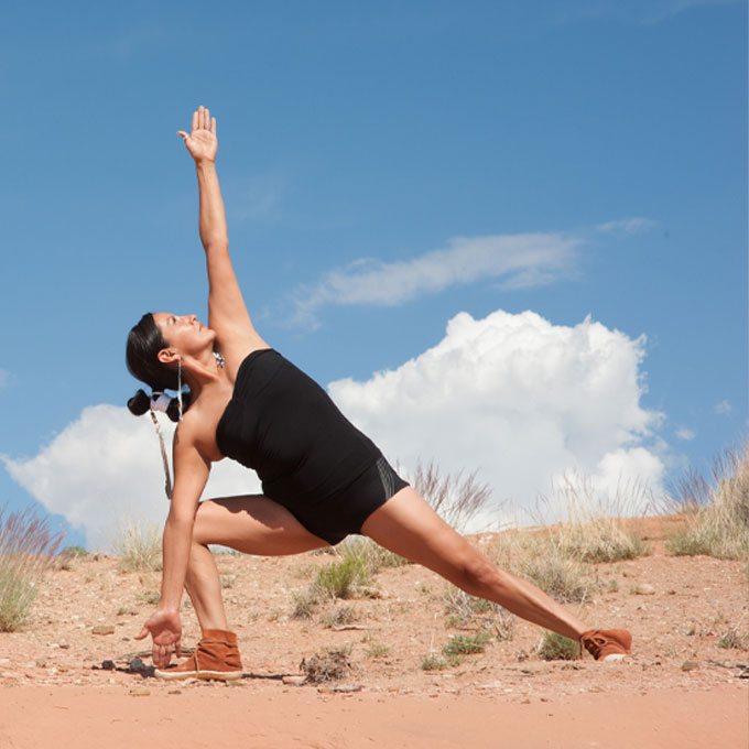 Eine Frau macht eine Yoga-Pose auf sandigem Boden unter blauem Himmel