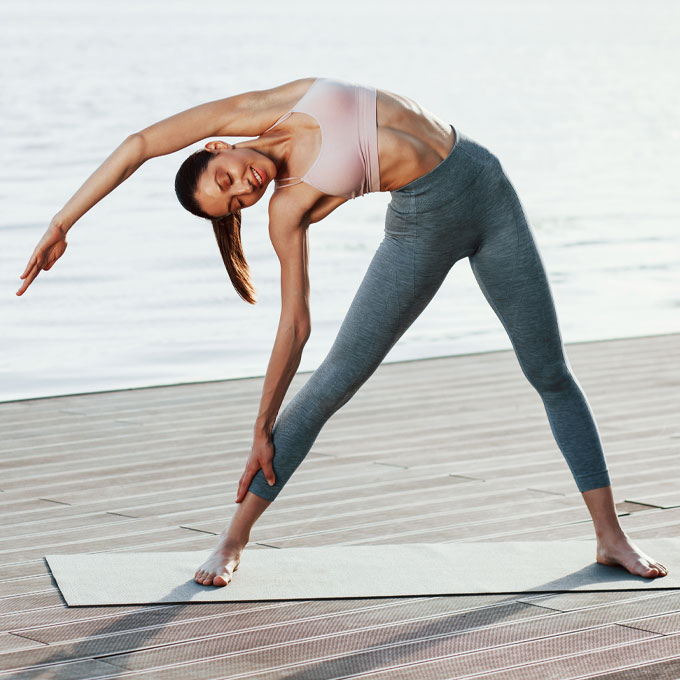 Frau macht Yogaübung auf einer Matte am Wasser