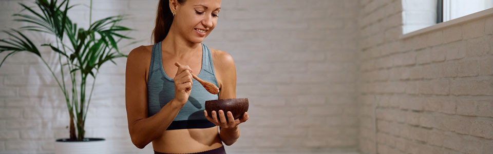 Frau beim Mischen mit Holzschale Frau in Sportkleidung mischt etwas in einer Holzschale mit einem Löffel
