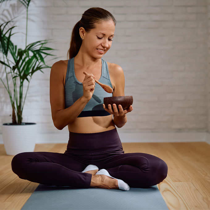 Frau im Yogasitz hält eine Schüssel und lächelt.