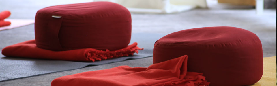 Zwei rote Meditationskissen auf Matten mit roten Decken im Hintergrund.