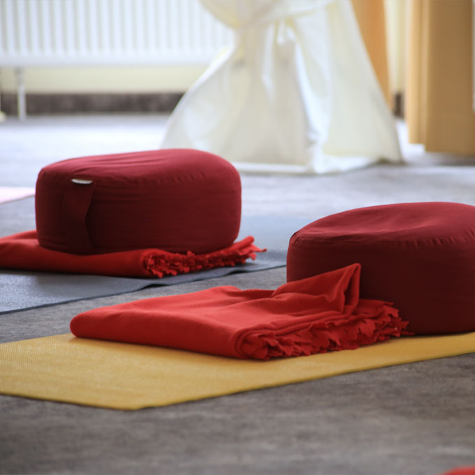 Zwei rote Meditationskissen und Decken auf gelben Matten.