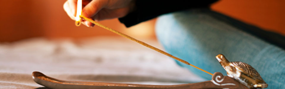 Hand zündet ein Räucherstäbchen in einem verzierten Halter an