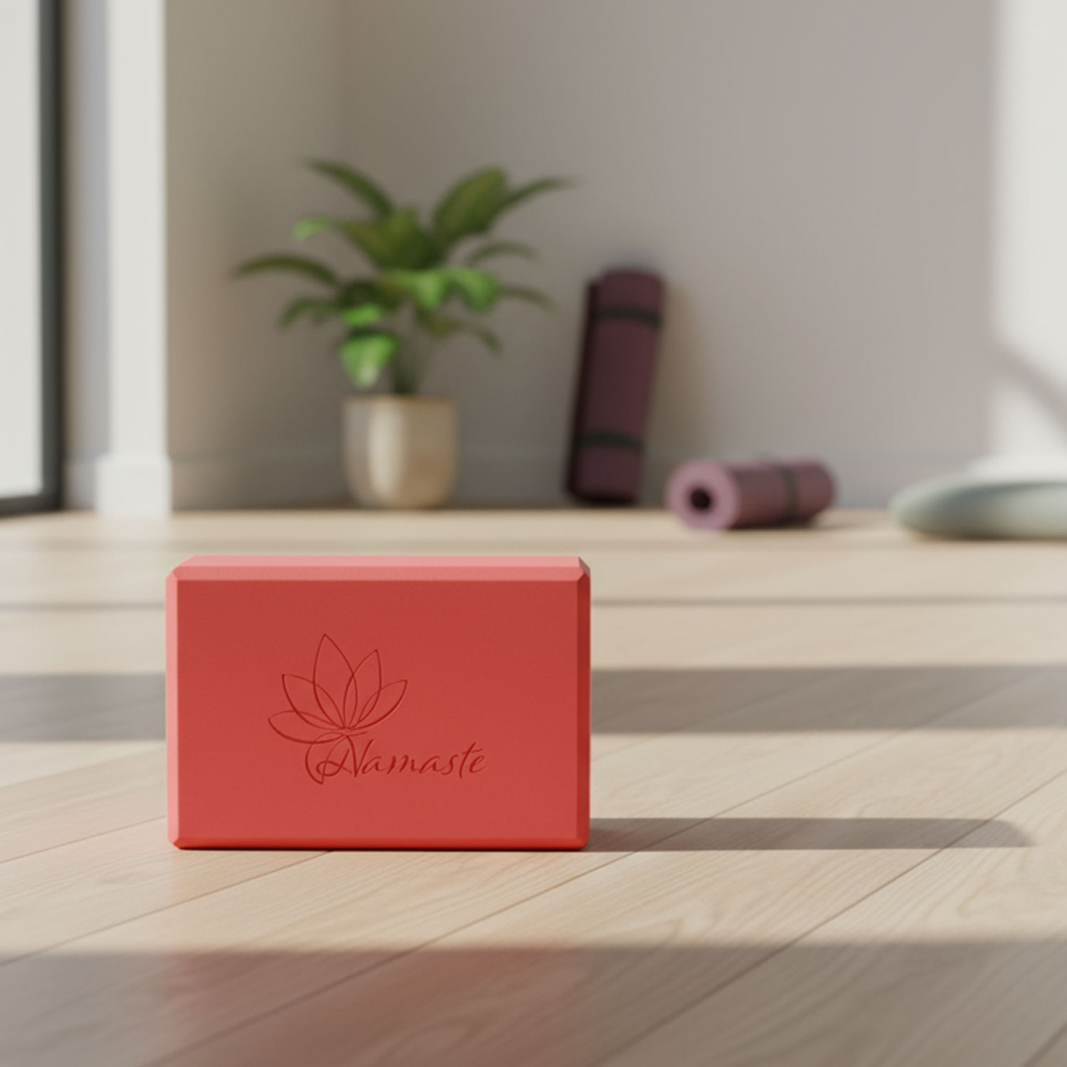 Ein roter Yoga-Block mit der Aufschrift 'Namaste' auf einem Holzboden, im Hintergrund Yoga-Matten und eine Pflanze.