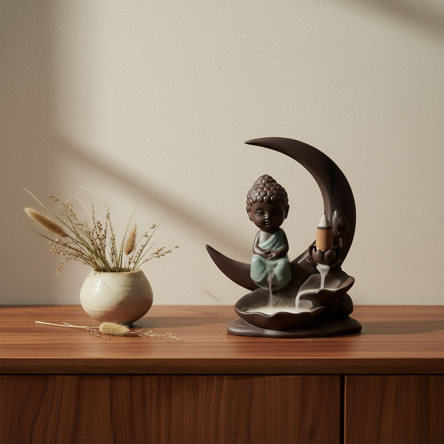 Kleine Buddha-Figur neben einer Vase mit Trockenblumen auf einem Holztisch.