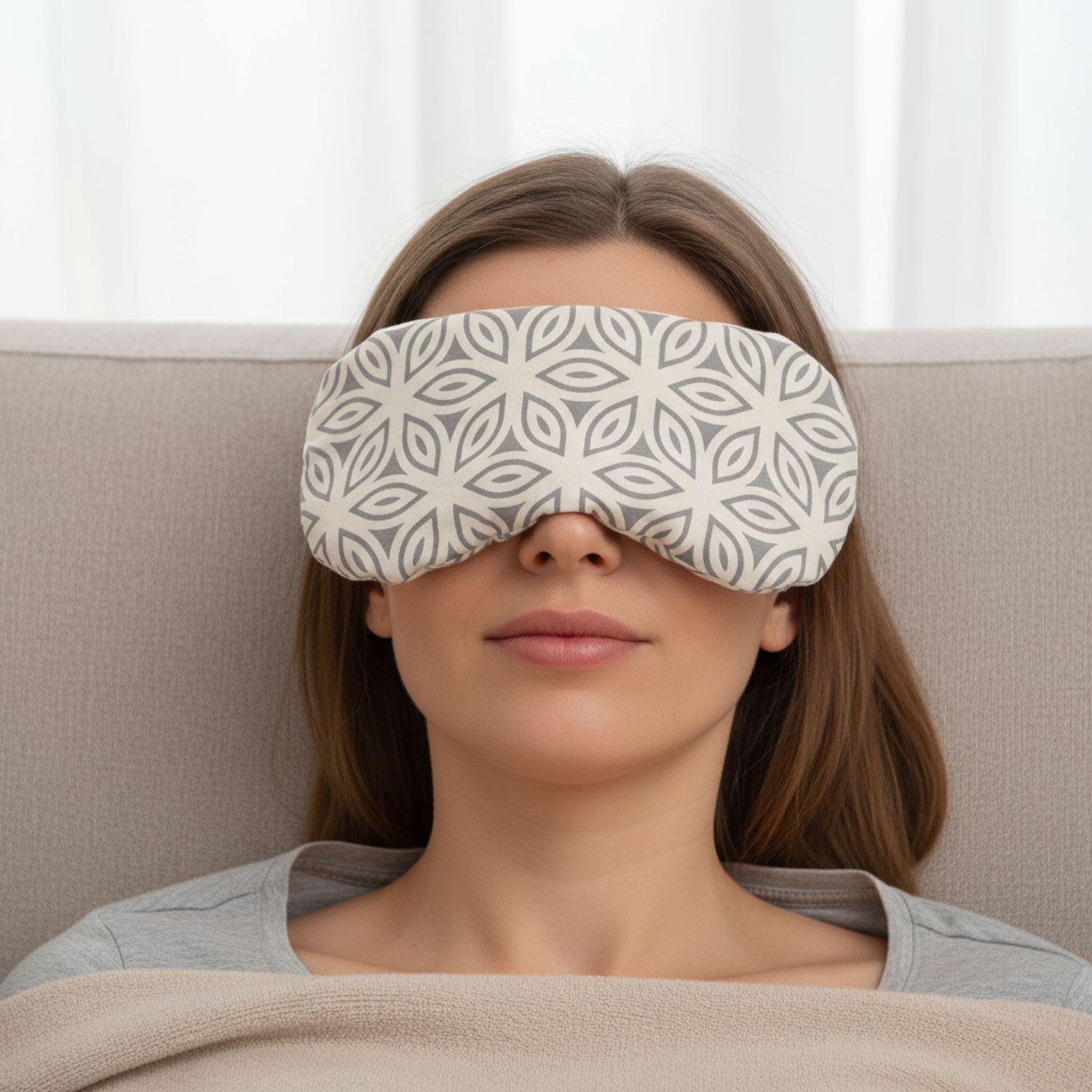Eine Frau liegt mit einer gemusterten Schlafmaske auf einem Sofa und entspannt.