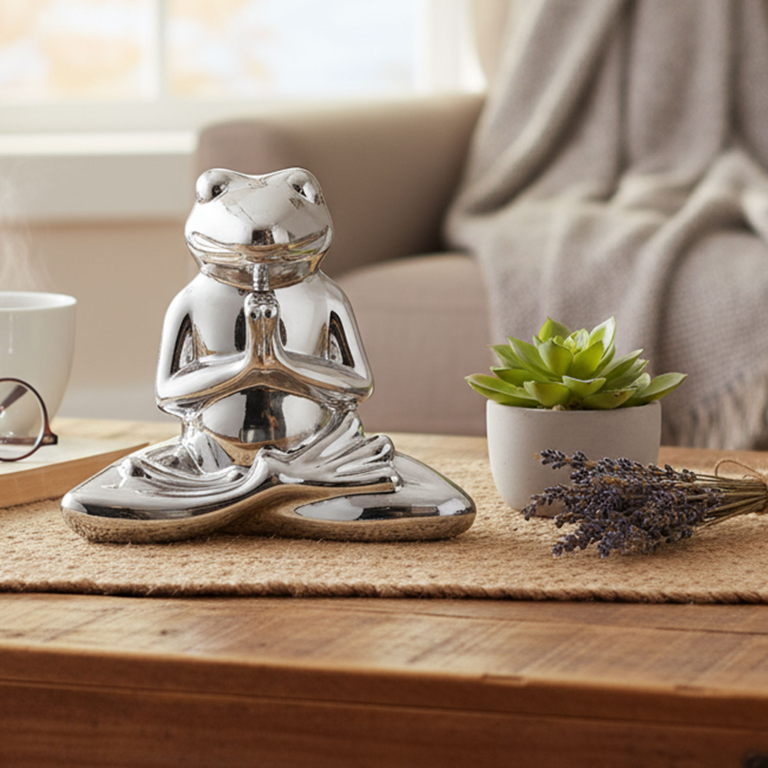 Silberne Froschstatue im Lotussitz neben einer Pflanze auf einem Tisch