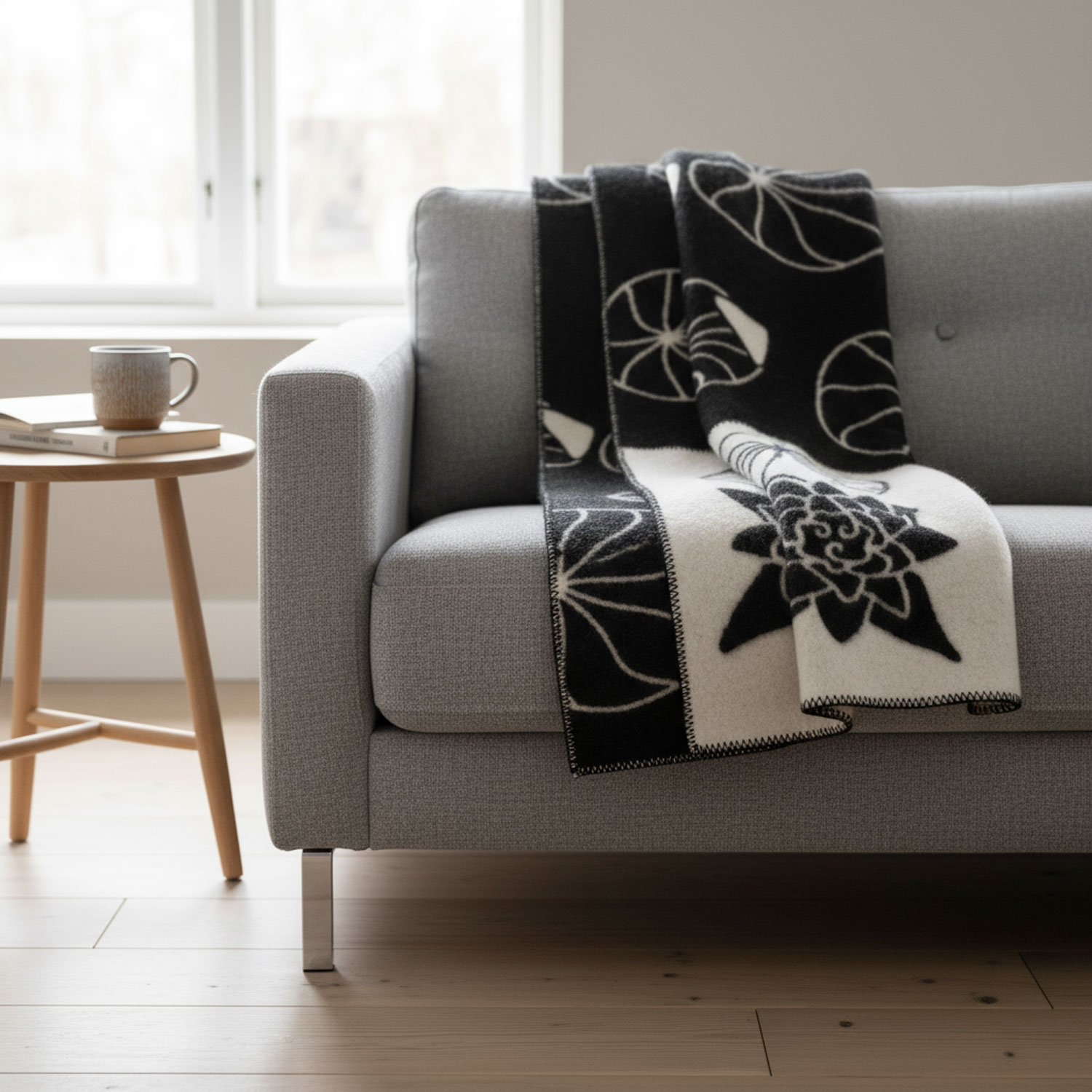 Graues Sofa mit schwarz-weißer Decke und Beistelltisch mit Tasse und Büchern