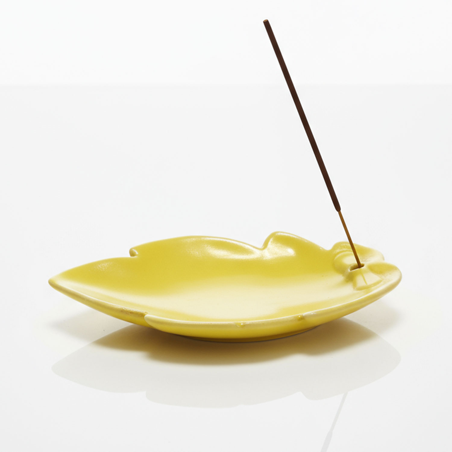 Ein gelber Räucherstäbchenhalter mit einem brennenden Räucherstäbchen.