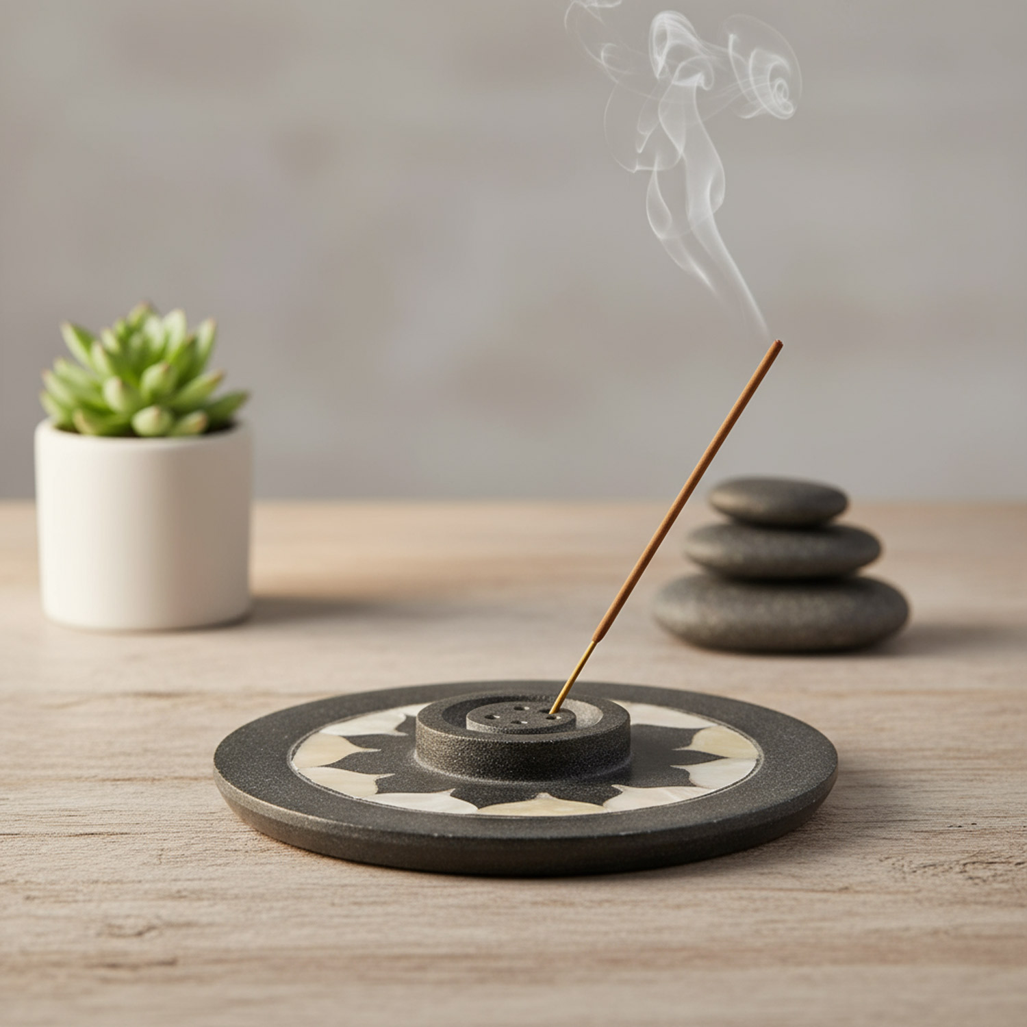 Ein brennendes Räucherstäbchen auf einem Halter, daneben Steine und eine Pflanze.
