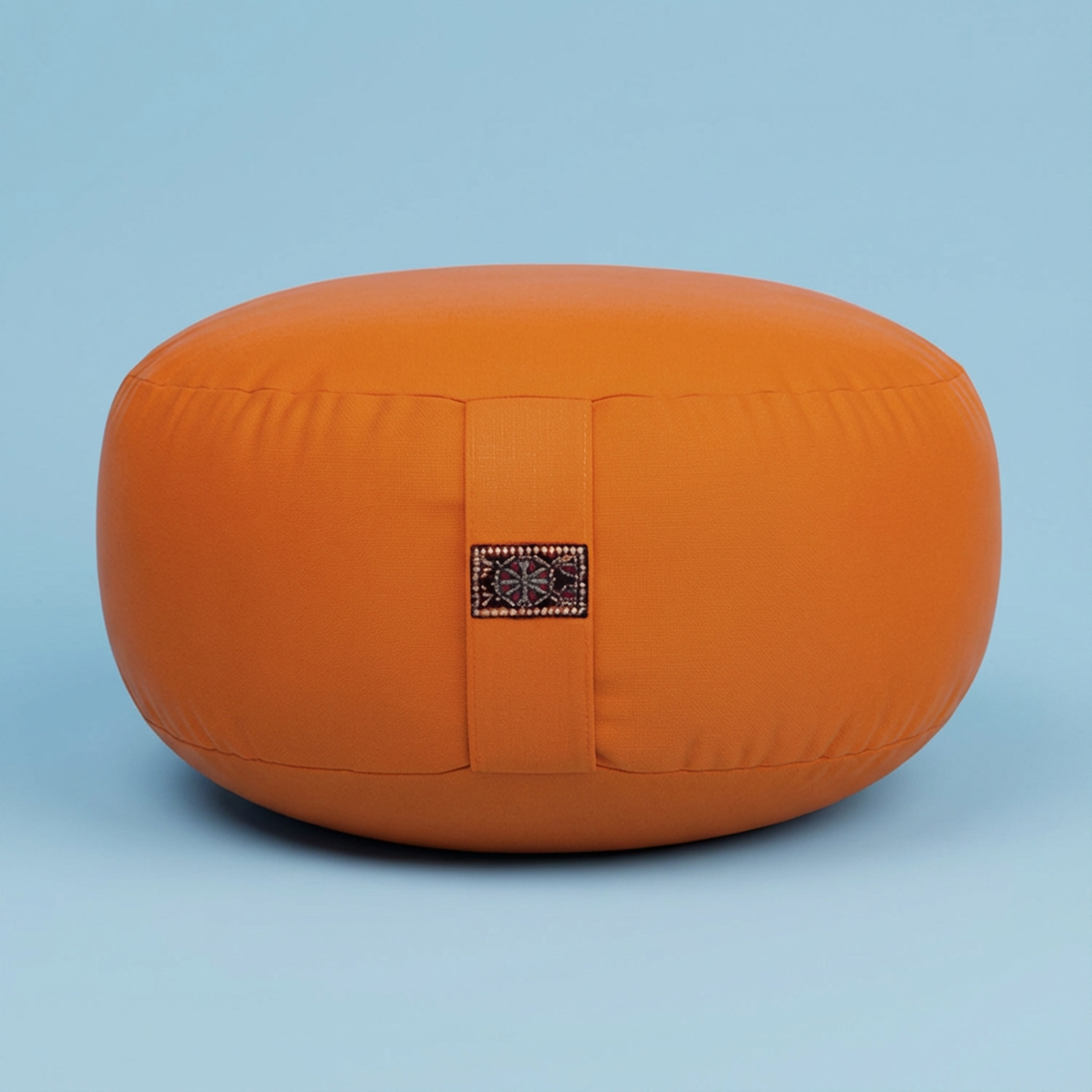 Ein rundes orangenes Meditationskissen mit einem dekorativen Band vor einem hellblauen Hintergrund.