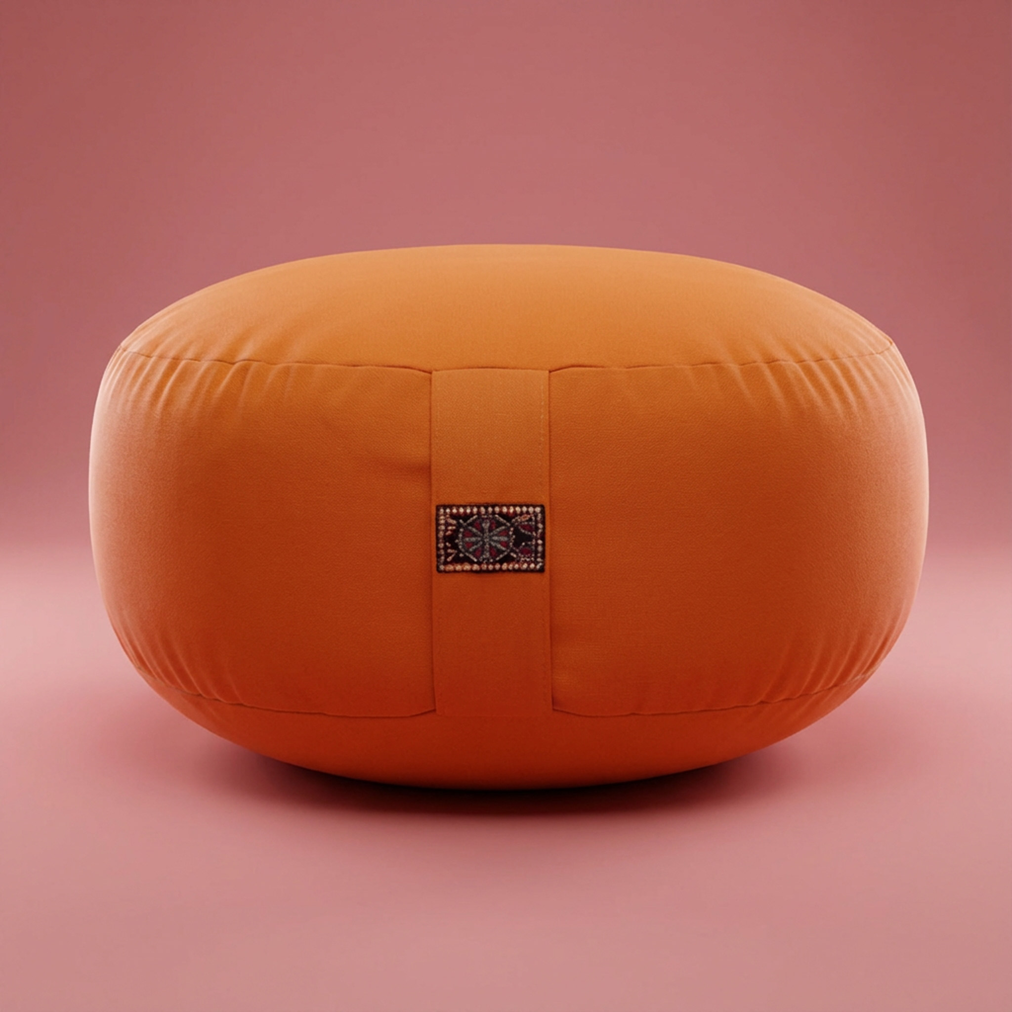 Ein rundes orangefarbenes Kissen mit Musterdetail vor einem rosa Hintergrund
