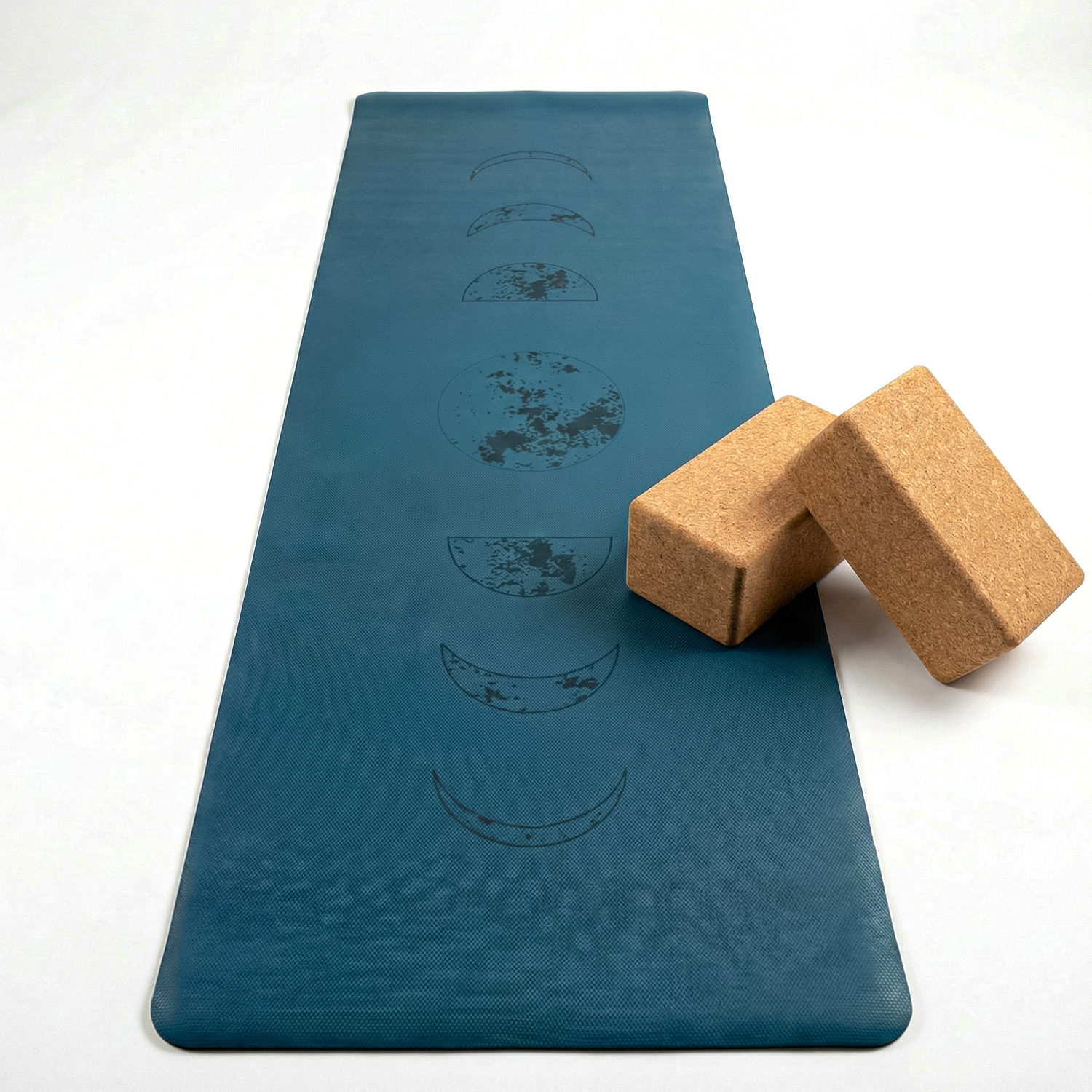 Petrol Yogamatte mit aufgedruckten Mondphasen und zwei Korkblöcken daneben