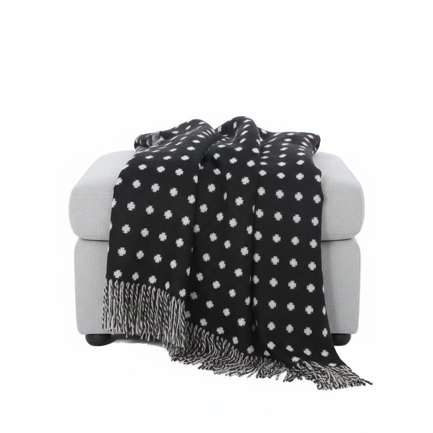 Ein hellgrauer Hocker, über den eine schwarze Decke mit weißen Punkten und Fransen gelegt ist.