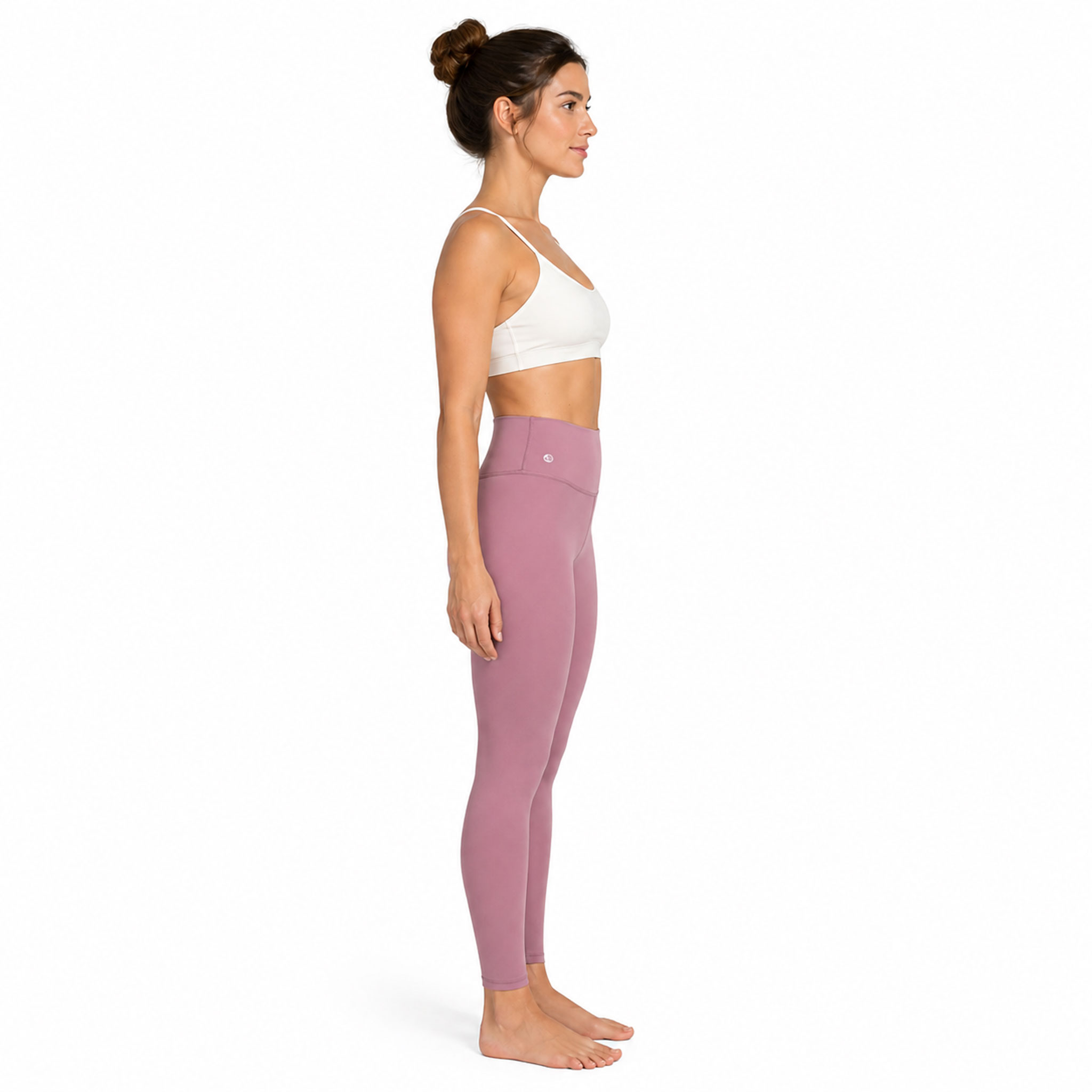 Eine Frau steht barfuß in Seitenansicht und trägt einen weißen Sport-BH sowie rosafarbene Leggings.