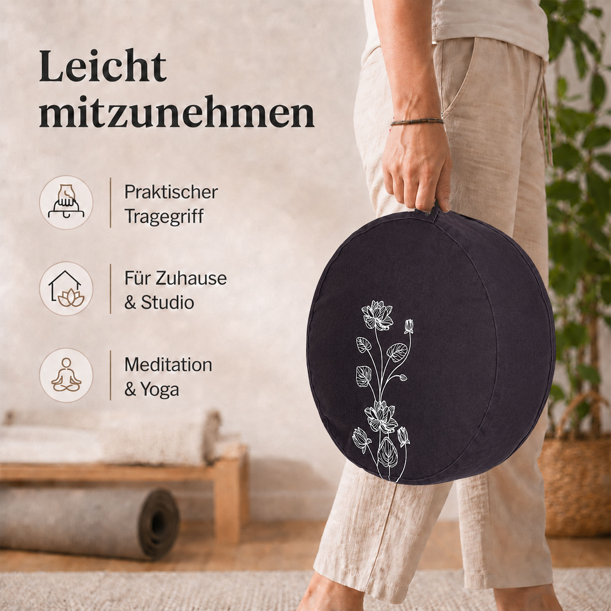 Person hält ein rundes Meditationskissen mit Blumenmotiv an einem Tragegriff in einer ruhigen Wohn- oder Studio-Umgebung.